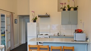 A compact kitchen with a central island, a refrigerator, a stove, and a microwave. There are three wooden chairs at the island, and the kitchen has a light blue backsplash.
