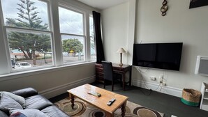 A living room with a sofa, a wooden coffee table, a TV, and a window with a view of trees and a car.