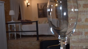 Ein Weinglas auf einem Tisch in einem Raum mit Backsteinwand, Holzbalken, einem Bett und einem kleinen Tisch mit einer Lampe.