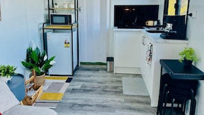 A compact kitchen with a refrigerator, microwave, and coffee machine. There is a small dining area with a table and chairs. - Tiny Home in Hampton (Hampton)