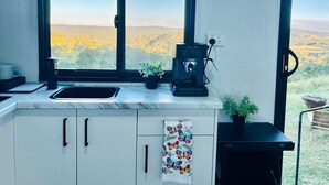 A kitchen with a large window, a coffee machine, and a view of a forested landscape. - Tiny Home in Hampton (Hampton)