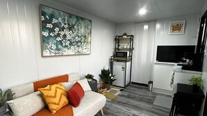 A modern living room with a sofa, a coffee table, a TV, and a kitchen area with a microwave. - Tiny Home in Hampton (Hampton)