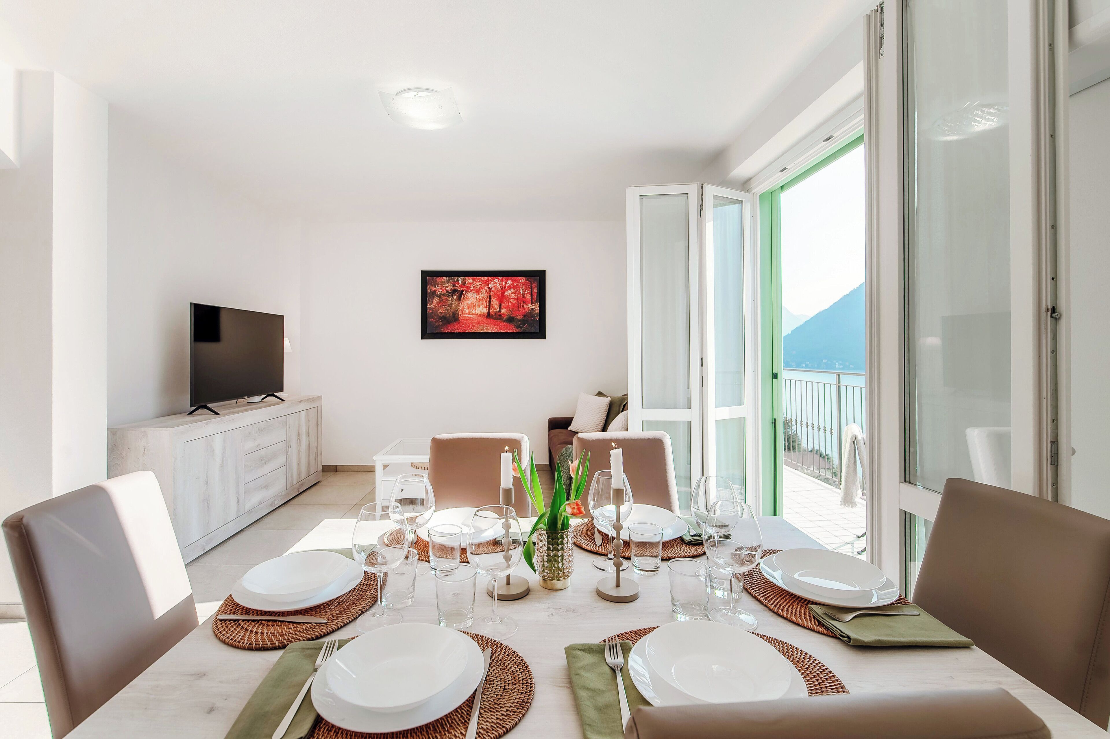 A dining area with a table set for four, a TV on a cabinet, and a painting on the wall.