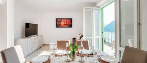 A dining area with a table set for four, a TV on a cabinet, and a painting on the wall.