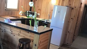 A wooden cabin kitchen with a central island, a refrigerator, and a window. - Persea House. Ideal for families and lovers of Bologna and its peace. (Tarifa)