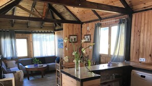 A cozy cabin interior with a wooden interior, a dining area, a kitchen, and a living room with a sofa and a coffee table. - Persea House. Ideal for families and lovers of Bologna and its peace. (Tarifa)