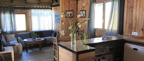 Interior acogedor de una cabaña con paredes de madera, un comedor, una cocina y una sala de estar con un sofá y una mesa de centro.