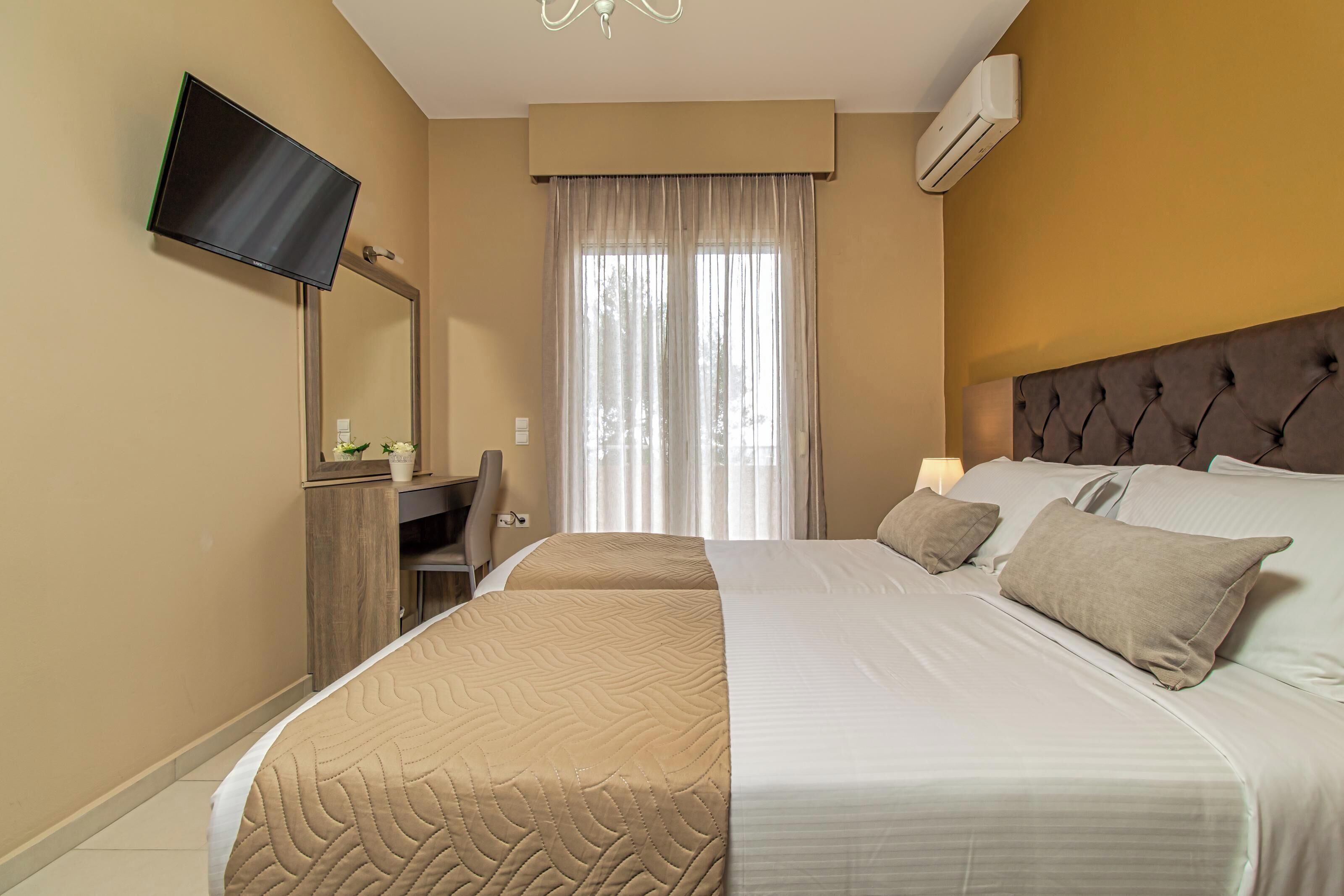 A hotel room with a large bed, a desk, a chair, a television mounted on the wall, and a window with curtains.