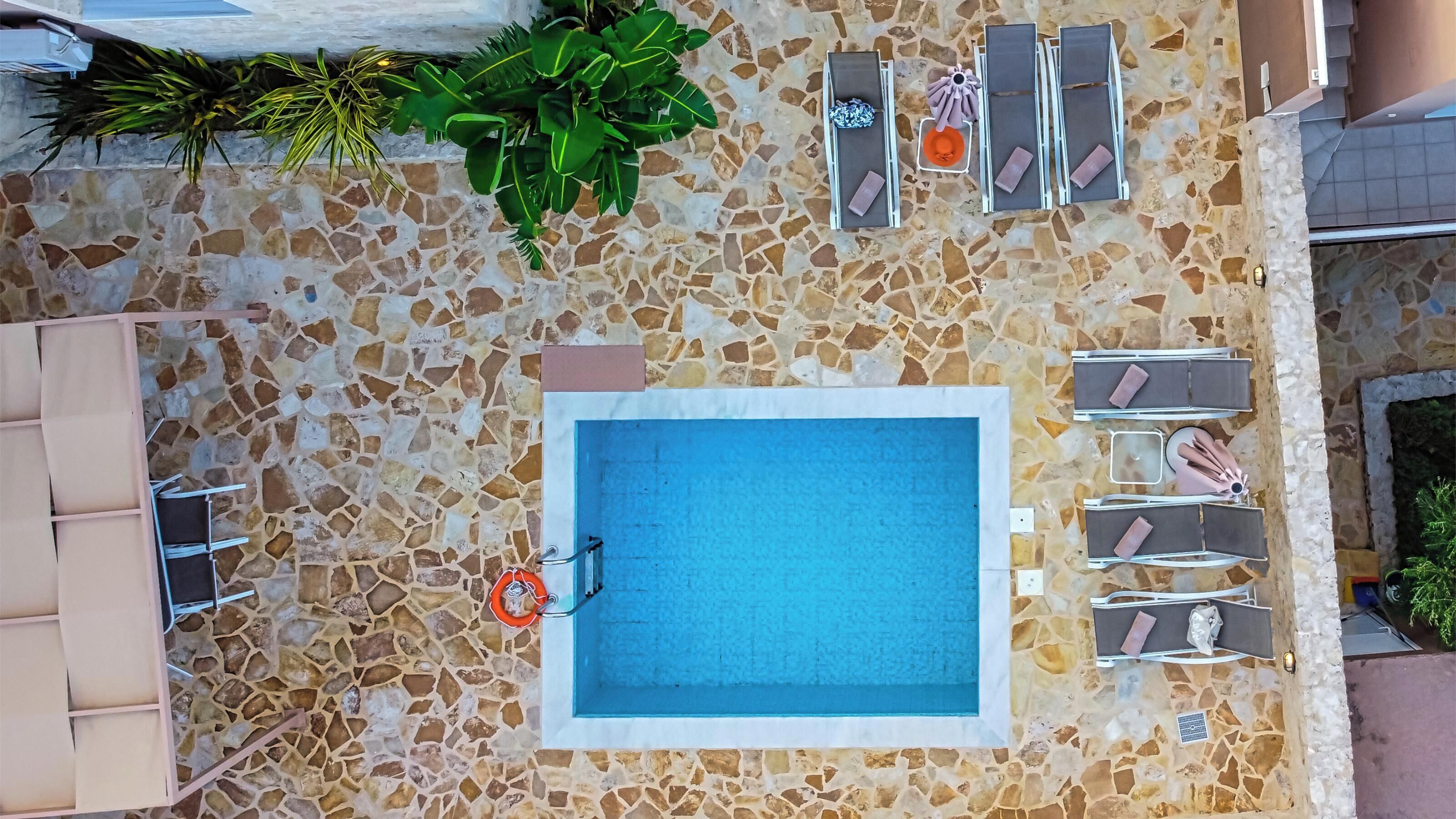 A rooftop pool with a stone-tiled deck, surrounded by lounge chairs and a small table with a drink umbrella.