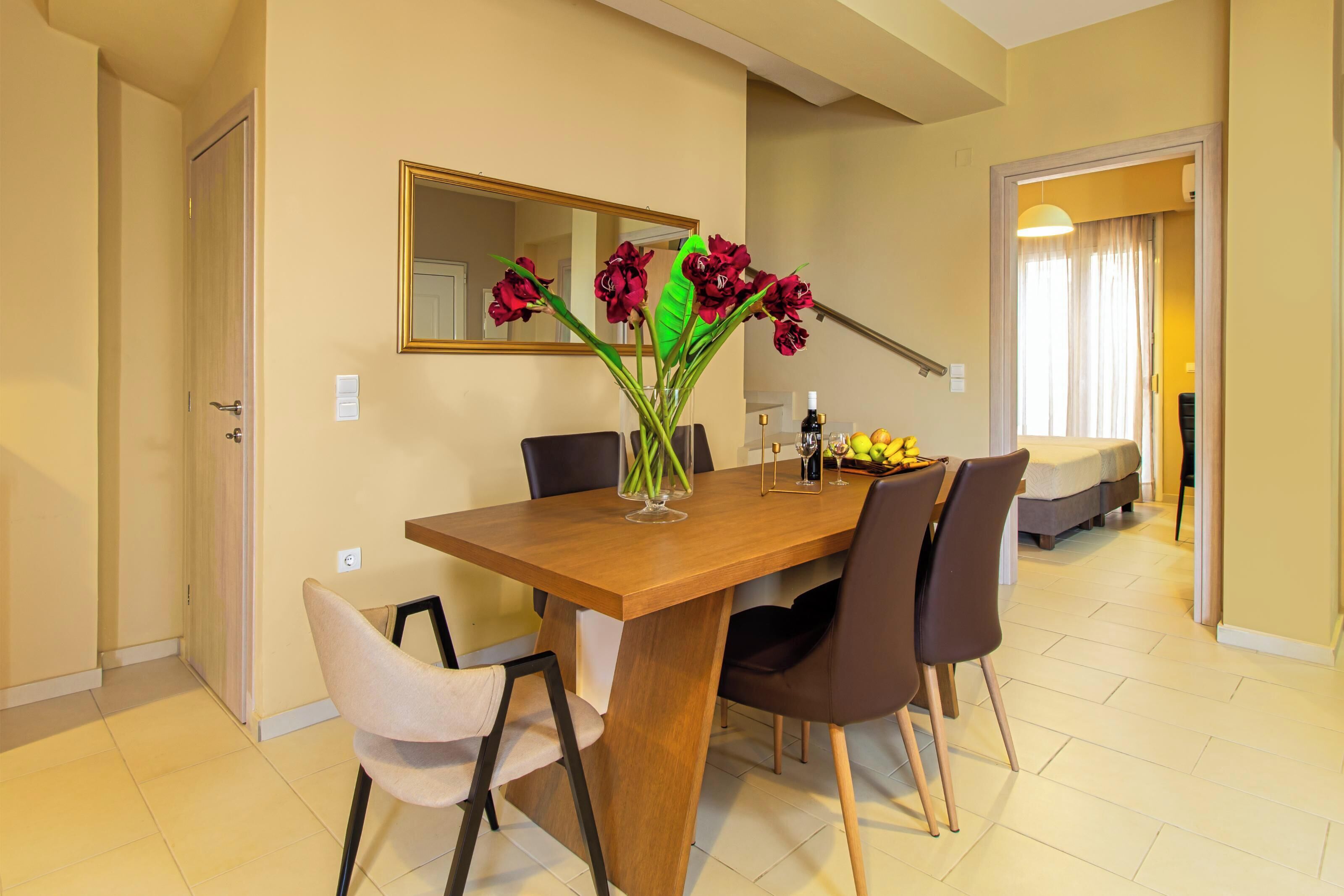 Un comedor con mesa de madera, cuatro sillas, un jarrón con flores y un espejo en la pared.