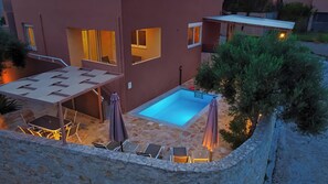 A modern building with a swimming pool, outdoor seating, and a stone wall. - Theo Villas With Sea View (Marathokefala)