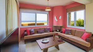 Un salon avec un canapé beige, une table basse et une cheminée. De grandes fenêtres offrent une vue sur l’extérieur.