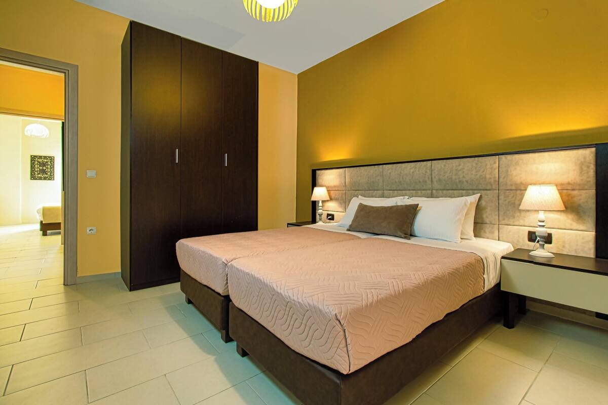 Une chambre d’hôtel avec un grand lit, deux tables de chevet avec des lampes, une armoire et une porte donnant sur une autre pièce.