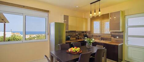 A modern kitchen with a dining area, large windows, and a view of the sea.
