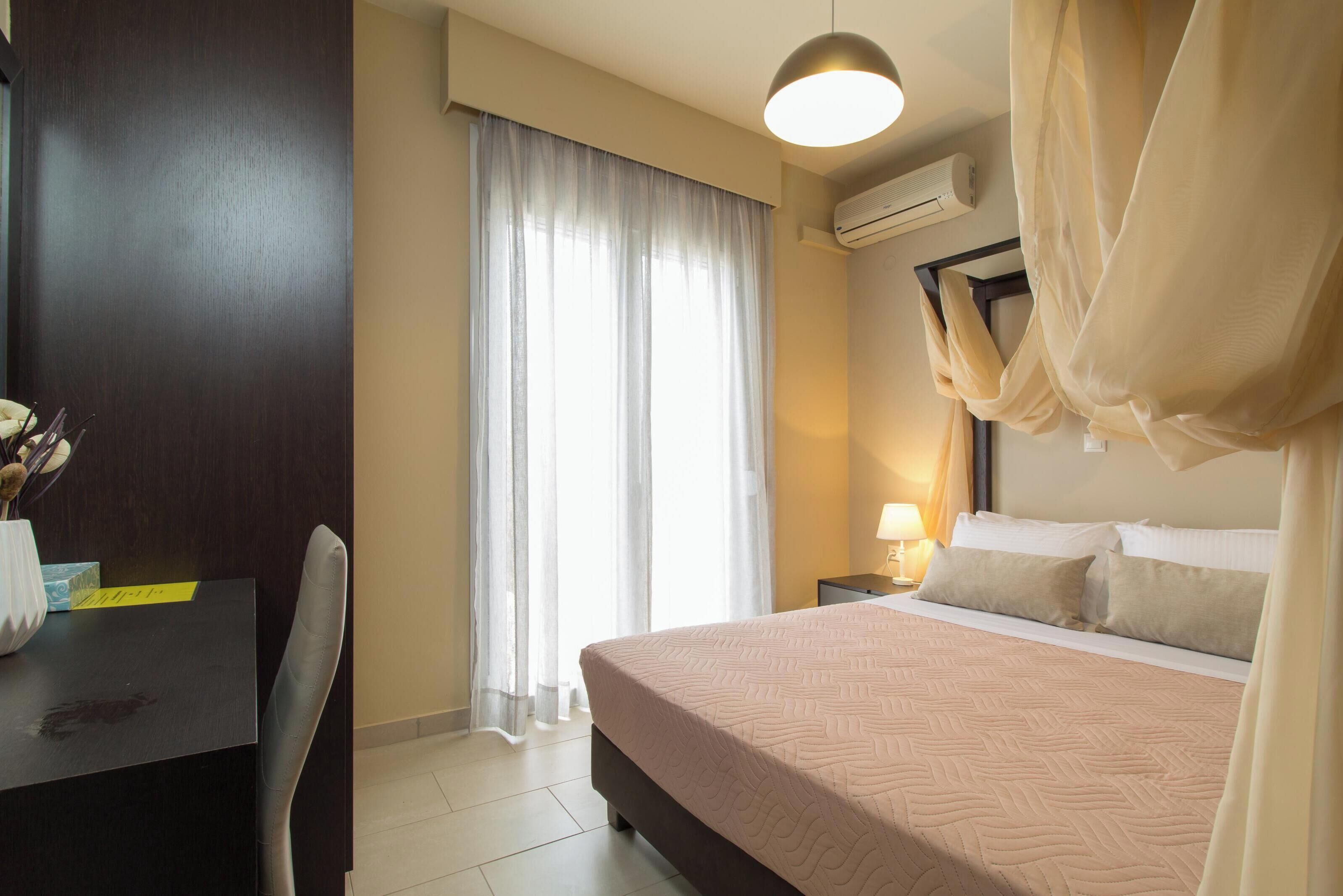 A hotel room with a bed, a desk, a chair, a lamp, and a window with curtains.