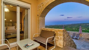 Un balcon orné d’une arche en pierre, une porte vitrée donnant sur une chambre, une table avec un magazine et une vue sur la campagne.