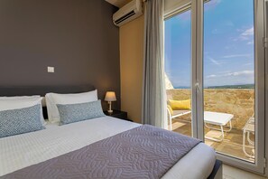 A hotel room with a large bed, a nightstand, a lamp, and a view of the outdoors through a sliding glass door. - Theo Villas With Sea View (Marathokefala)