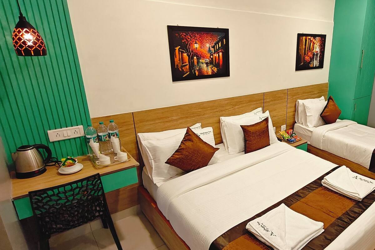 A hotel room with two beds, a desk with a kettle, a chair, and artwork on the walls.