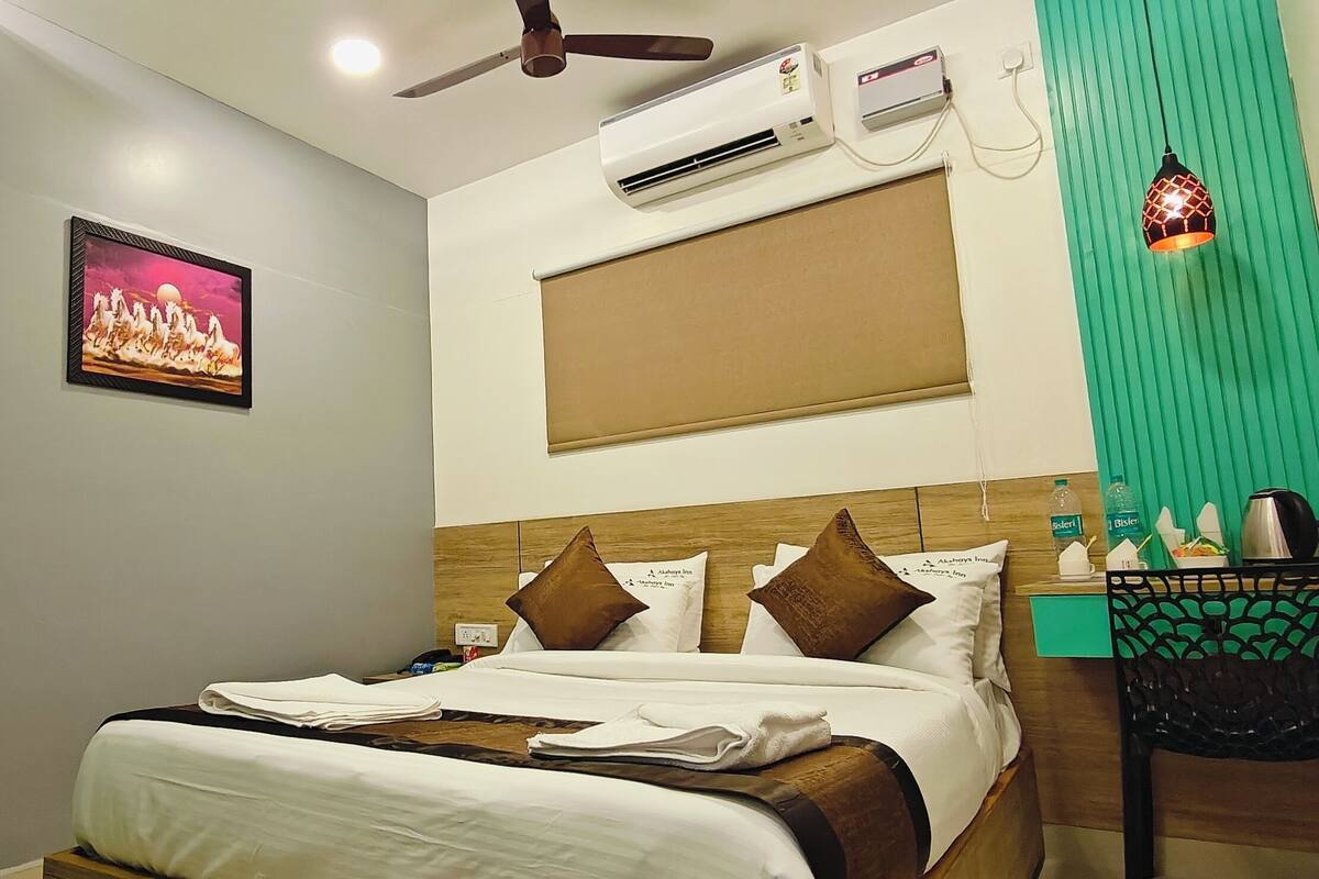 A hotel room with a bed, a nightstand, a desk, a chair, an air conditioning unit, a ceiling fan, a picture on the wall, and a window with blinds.