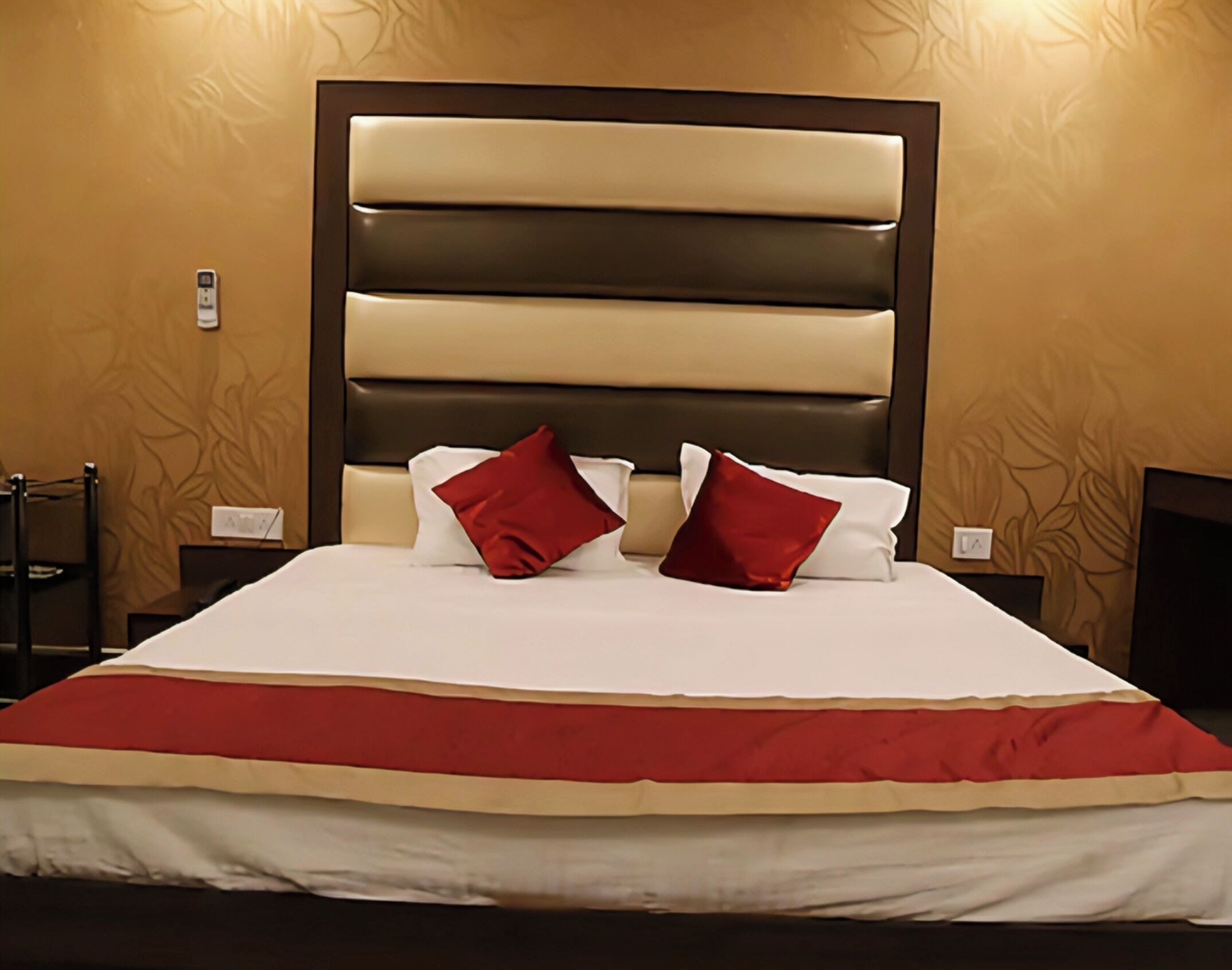 Habitación de hotel con una cama grande, dos almohadas rojas, una colcha blanca y un cabecero marrón.