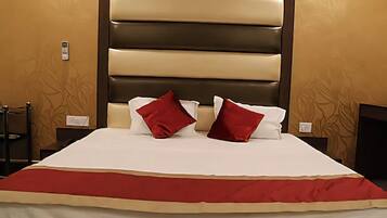 Habitación de hotel con una cama grande, dos almohadas rojas, una colcha blanca y un cabecero marrón.