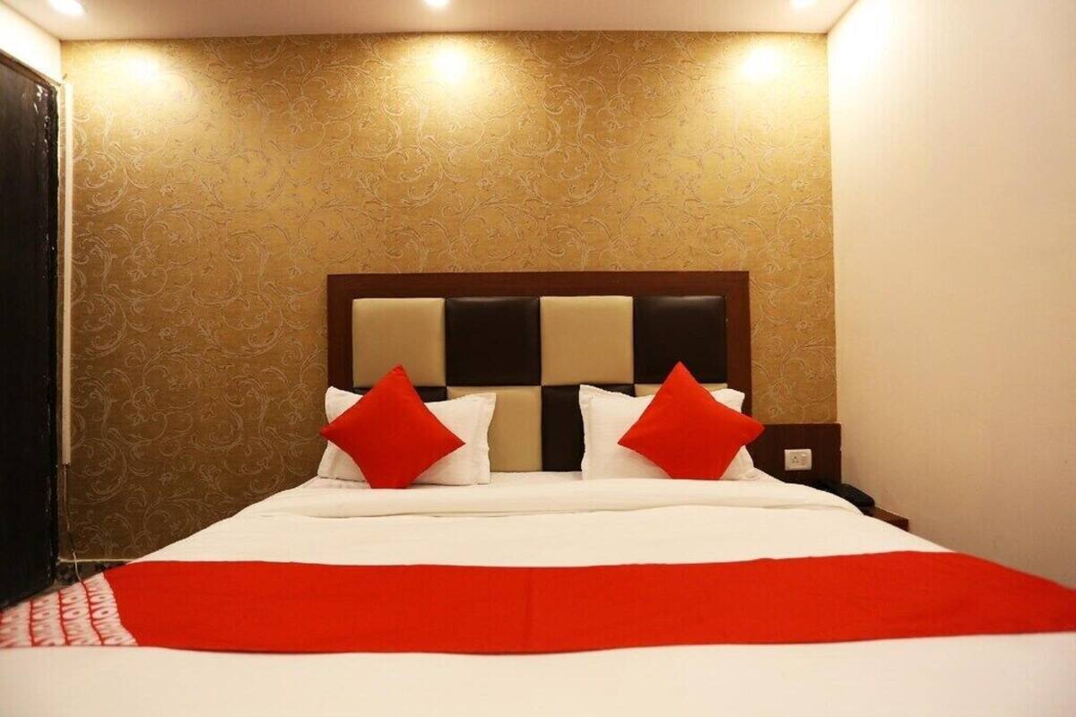 A hotel room with a large bed, a headboard with a checkered pattern, and a red and white bedspread.