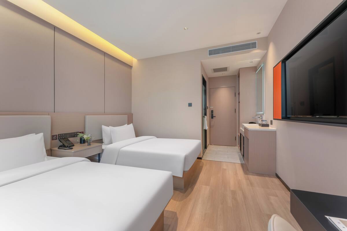 Habitación de hotel con dos camas, un escritorio con teléfono, televisor y kitchenette.