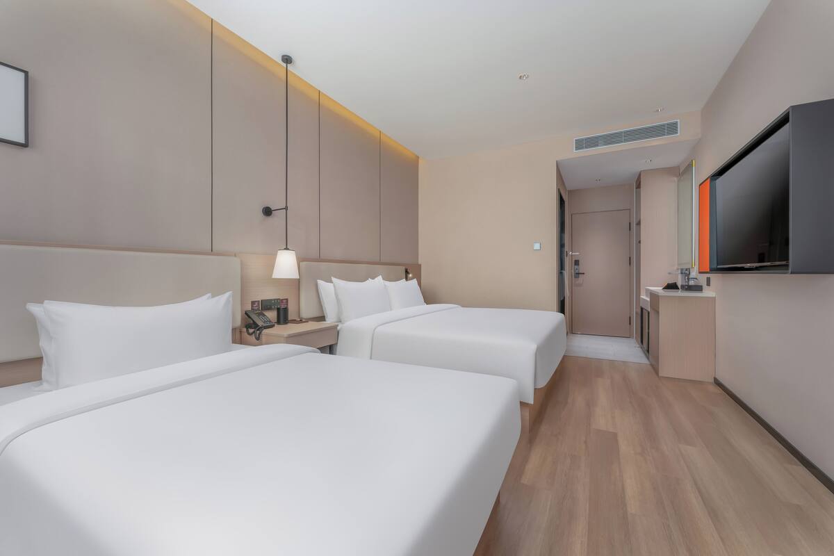 Habitación de hotel con dos camas, un escritorio, un televisor y un baño visible al fondo.