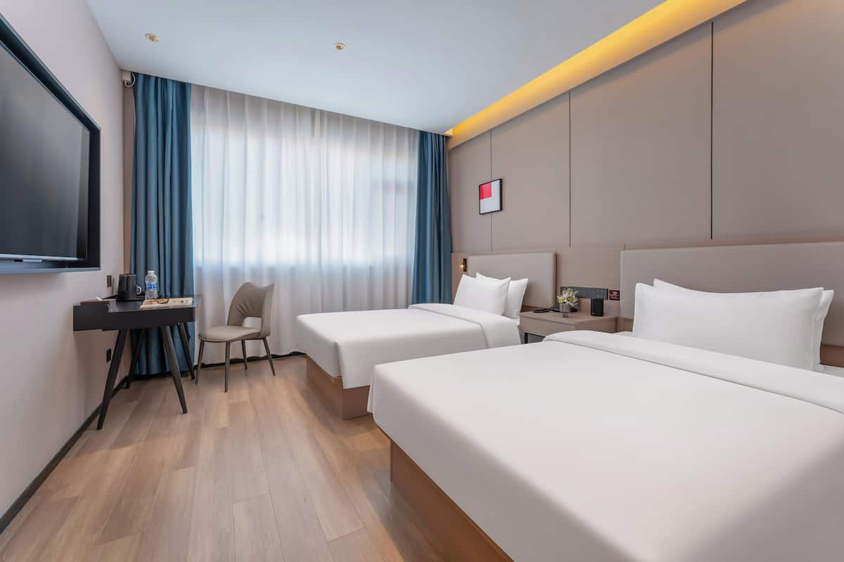 Habitación de hotel con dos camas, un escritorio con silla, televisión y ventana con cortinas.