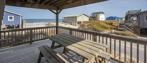 A wooden deck with a picnic table and a railing overlooking a beach with houses in the background.