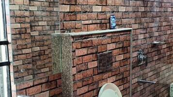 Un baño con pared de ladrillo, un lavabo blanco, un inodoro y una ducha.