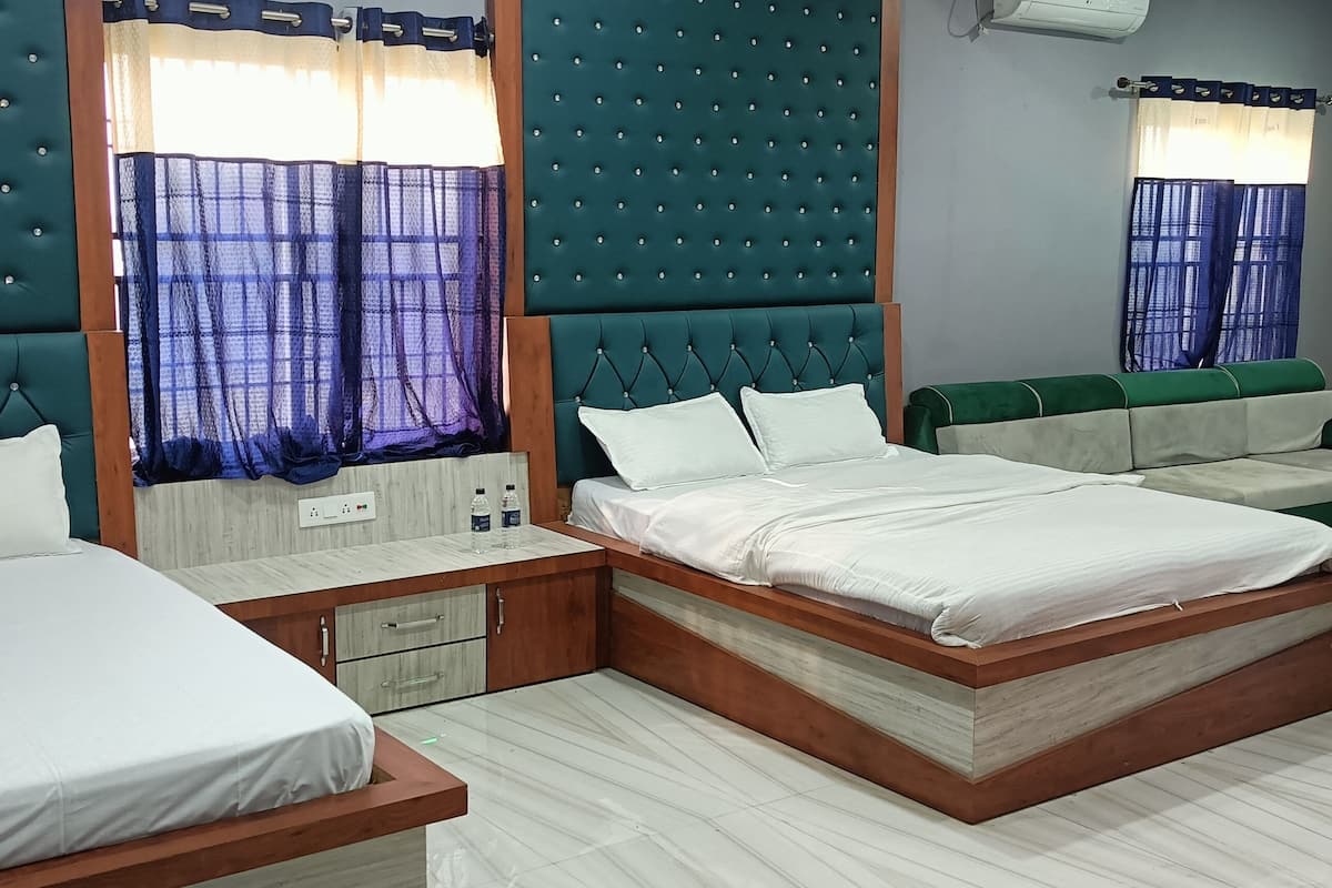 A hotel room with two beds, a green upholstered headboard, a wooden nightstand, and a small seating area with a green upholstered sofa.