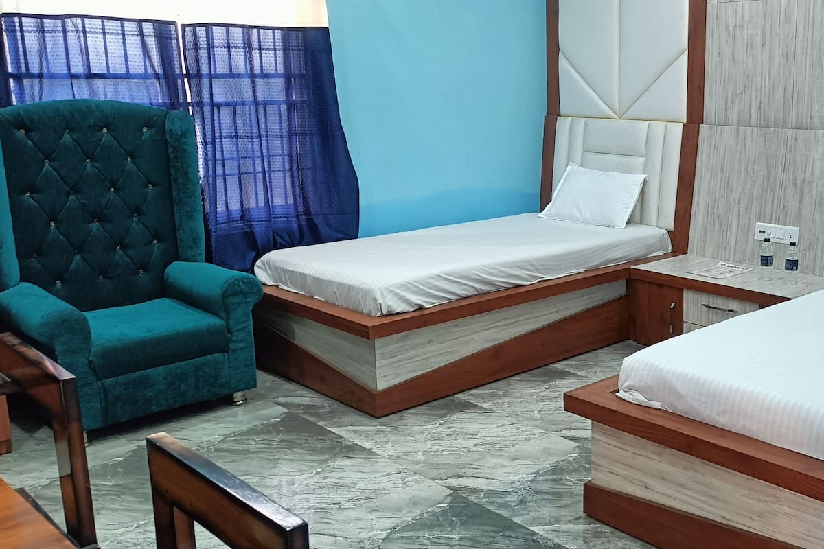 A hotel room with two beds, a teal armchair, a wooden nightstand, and a blue curtain.