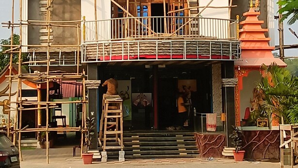 A building under construction with scaffolding, a blue window, and a small shrine-like structure with statues. - Hotel Sunjukti by Roh (Nagaon)