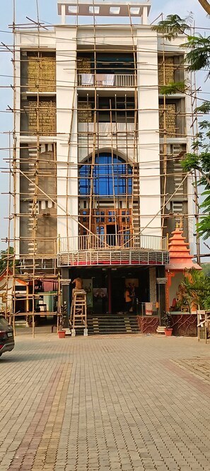 A building under construction with scaffolding, a blue window, and a small shrine-like structure with statues. - Hotel Sunjukti by Roh (Nagaon)