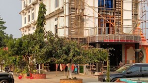 A multi-story building under construction with scaffolding, surrounded by trees and parked cars. - Hotel Sunjukti by Roh (Nagaon)
