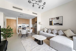 A modern living room with a grey sofa, a dining table, and a kitchen in the background. - Bayshore at Creek Beach 3 - 501 1BD (Dubai)