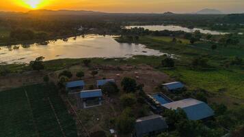 An aerial view of a rural area with several buildings, a river, and a sunset.