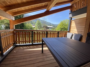 Eine Holzterrasse mit Tisch und Stühlen, einem Hollergeländer und Blick auf eine Berglandschaft.