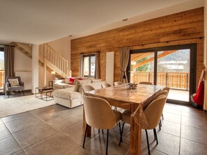 Ein großzügiger Wohnbereich mit Holzboden, einem Esstisch mit Stühlen, einer Sofagarnitur, einer Treppe und einem Balkon mit Blick.