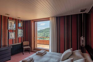 Une chambre à coucher avec un grand lit, une chaise, un bureau et une fenêtre donnant sur une zone boisée.