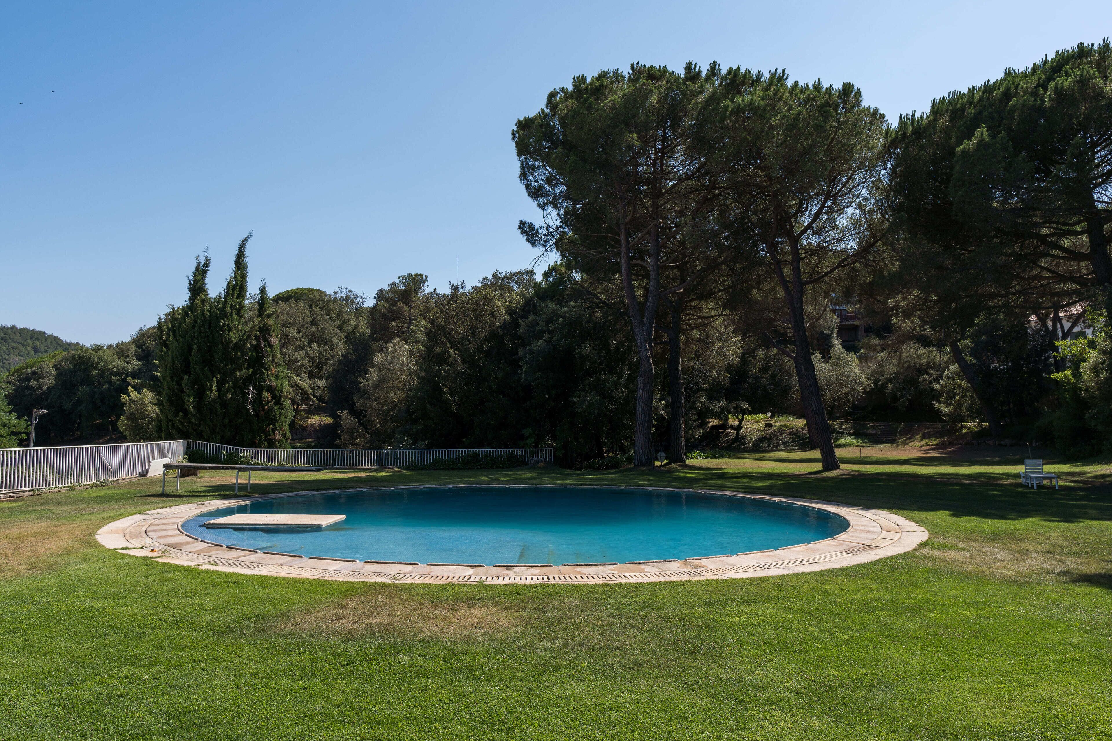 Une piscine ronde entourée d’une terrasse en pierre, elle-même bordée d’une pelouse verdoyante et d’arbres.
