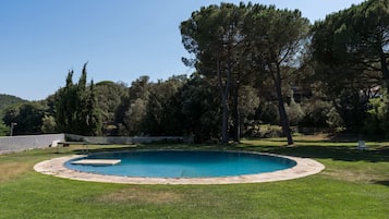 Une piscine ronde entourée d’une terrasse en pierre, elle-même bordée d’une pelouse verdoyante et d’arbres.