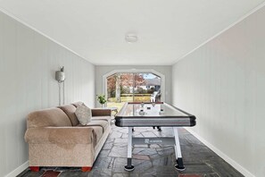 A room with a foosball table, a sofa, and a view of a garden.