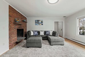 Un soggiorno con camino in mattoni, un divano angolare grigio, un tappeto decorato e un quadro appeso al muro.