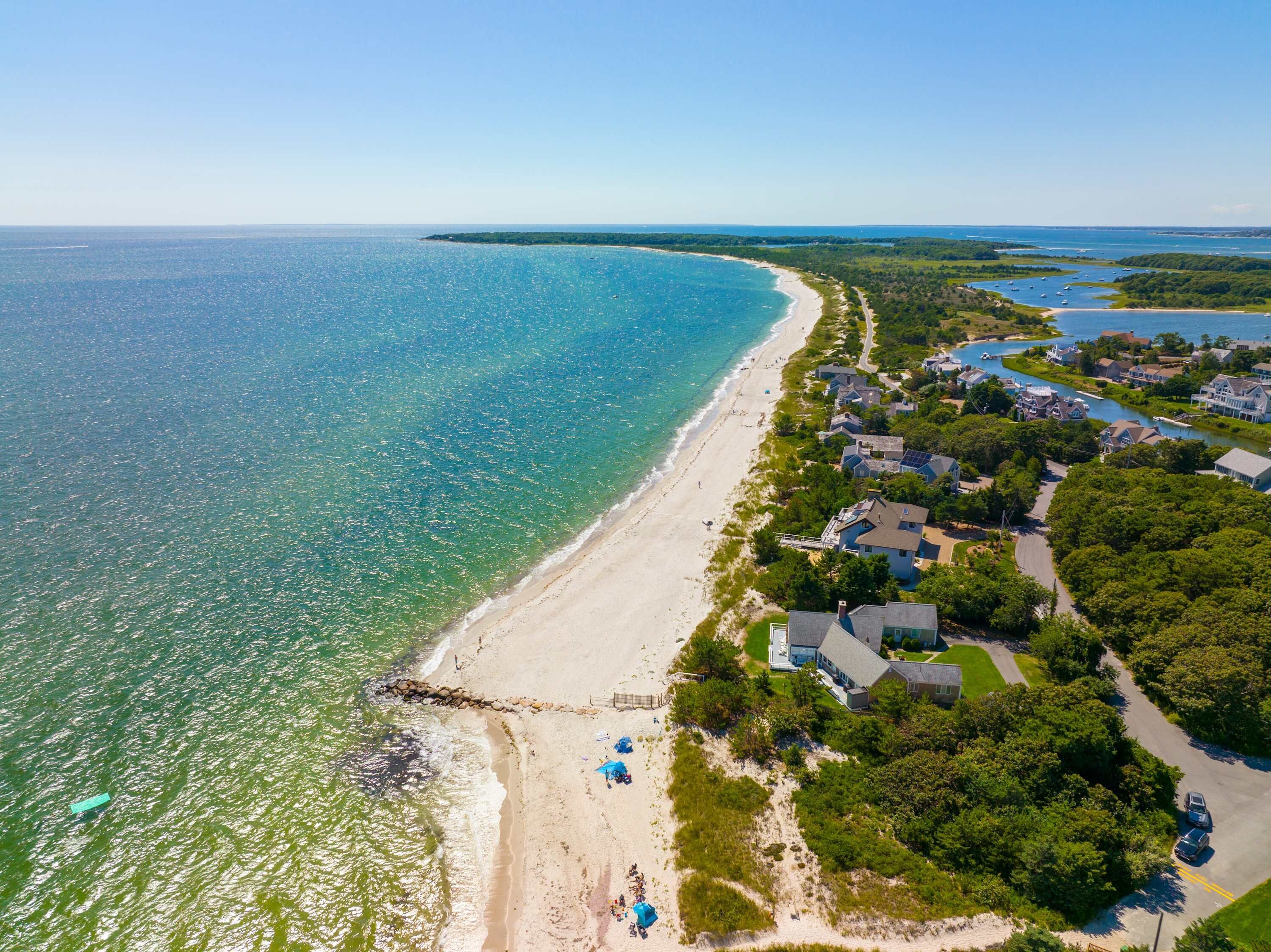 An aerial view of a coastal area with a beach, houses, and a road.