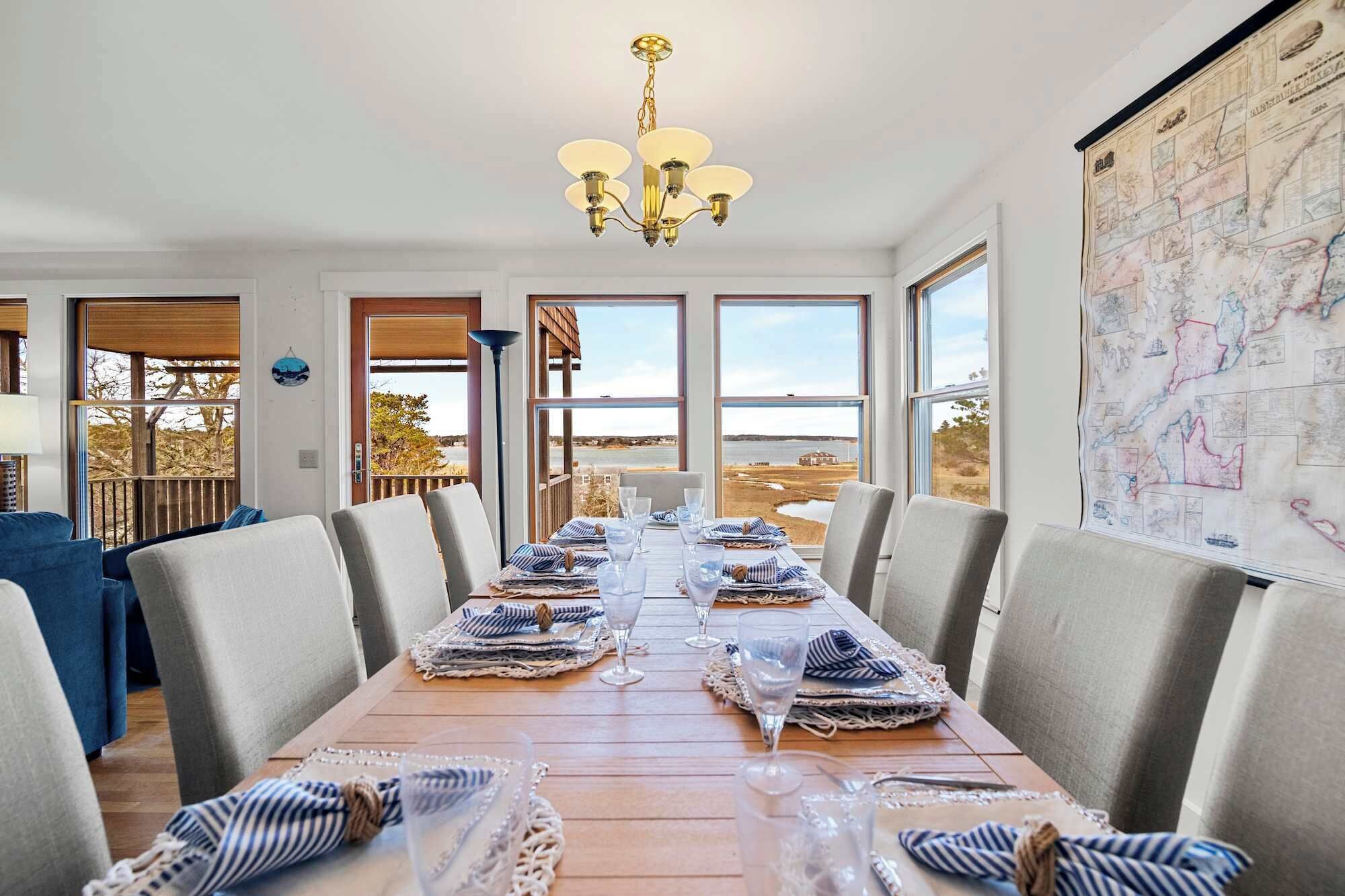 A dining room with a long table set for six, large windows, and a map on the wall.