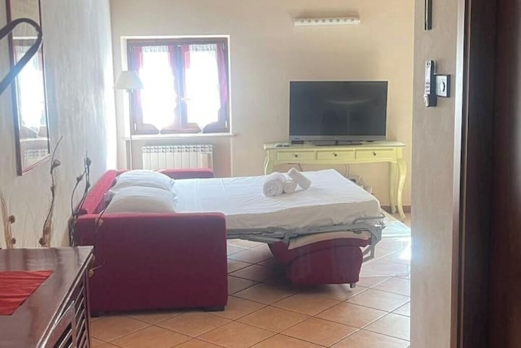 Een slaapkamer met een bed, een televisie op een standaard, een raam met gordijnen en een radiator.
