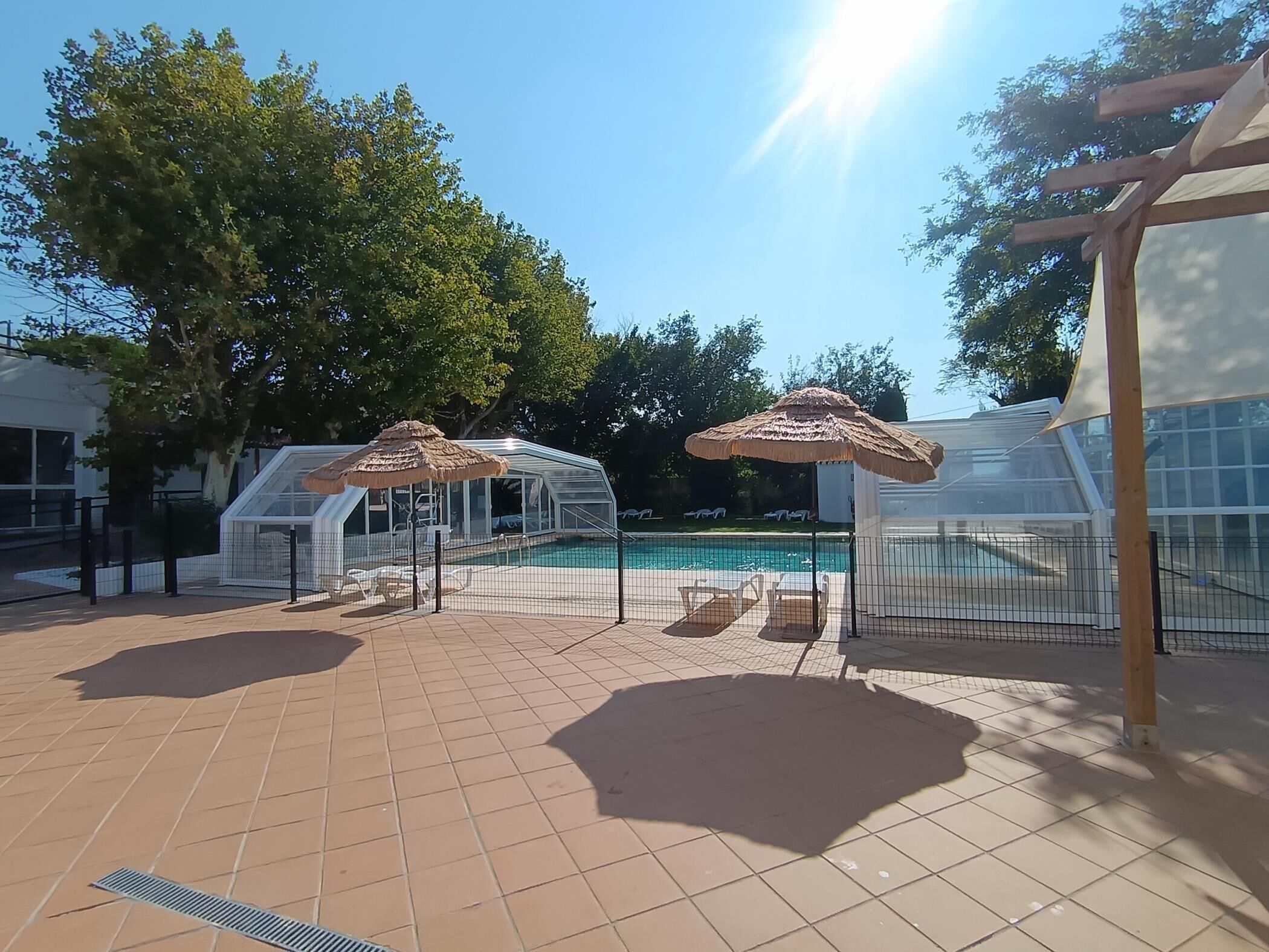 A swimming pool area with sun umbrellas, a covered seating area, and a fenced enclosure.