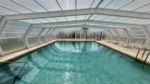 Una piscina con techo de vidrio, agua cristalina y sillones blancos a lo largo del borde.